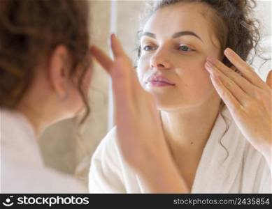 woman applying cream face while looking mirror 2