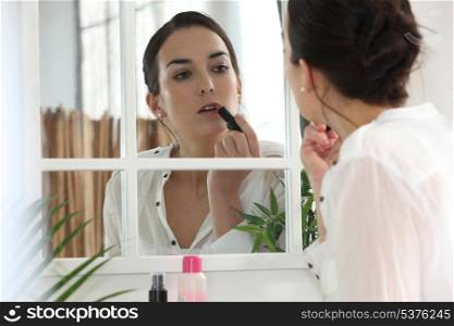 Woman applying lipstick face to the mirror