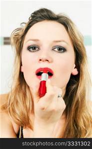 Woman applying lipstick on her lips looking at the viewer