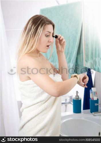 Woman applying makeup at bathroom being late and looking at watches