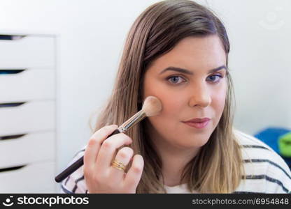 Woman applying makeup in her bedroom. She is smiling.