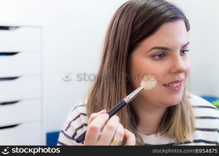 Woman applying makeup in her bedroom. She is smiling.