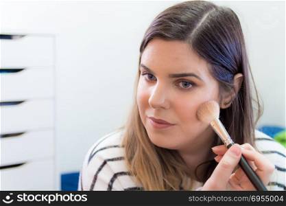 Woman applying makeup in her bedroom. She is smiling.