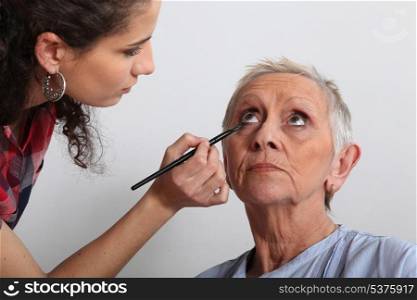 Woman applying makeup to an older lady