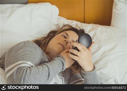 Woman applying makeup while she is lying on her bed