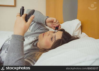 Woman applying makeup while she is lying on her bed