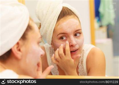 Woman applying mask cream on face in bathroom. Woman applying mask moisturizing skin cream on face looking in bathroom mirror. Girl taking care of her complexion layering moisturizer. Skincare spa treatment.