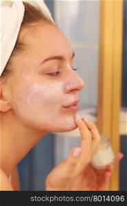 Woman applying mask cream on face in bathroom. Woman applying mask moisturizing skin cream on face looking in bathroom mirror. Girl taking care of her complexion layering moisturizer. Skincare spa treatment.