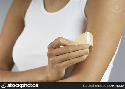 Woman applying patch to arm, mid section
