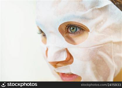 Woman applying sheet mask on her face. Girl taking care of skin complexion. Beauty treatment. Skincare.. Woman applying sheet mask on face