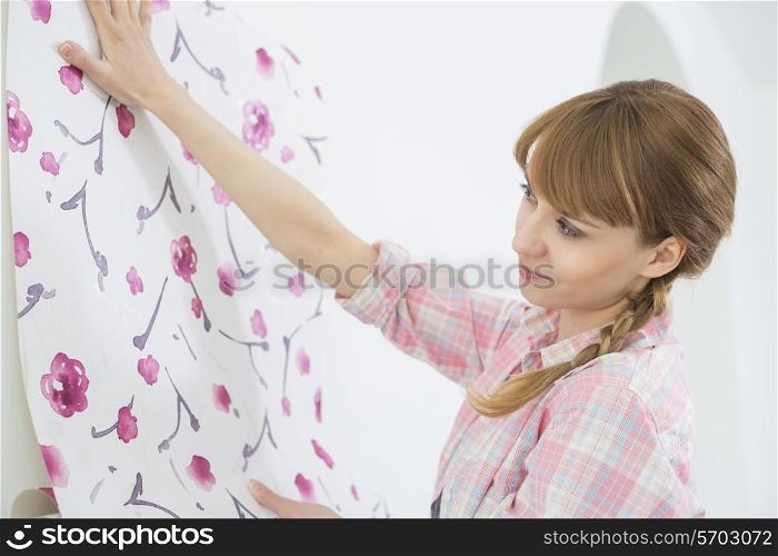 Woman applying wallpaper on wall in new house