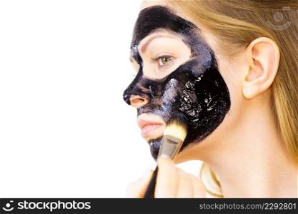 Woman applying with brush black detox mud mask to her face. Girl taking care of skin. Spa treatment. Skincare.. Woman applying black mask to skin face