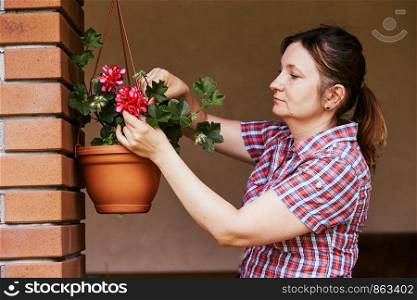 Woman arranging the flowers in a flower pot hanging on a patio. Candid people, real moments, authentic situations