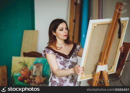 Woman artist painting a picture in a studio. Creative pensive painter girl paints a colorful picture on canvas with oil colors in workshop.