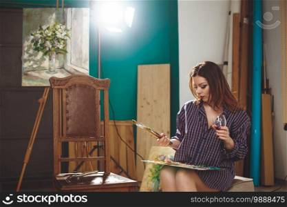 Woman artist painting a picture in loft studio. Creative pensive painter girl paints a colorful picture on canvas with oil colors in workshop. 