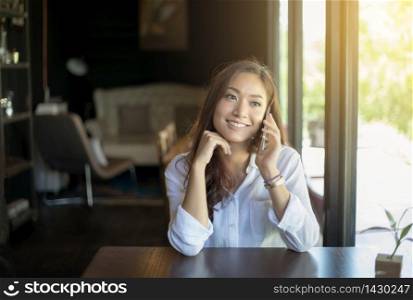 woman asian calling with cell telephone while sitting alone in coffee shop during free time