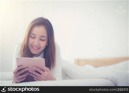 woman asian lying in bedroom with digital tablet touching with finger in morning sunlight