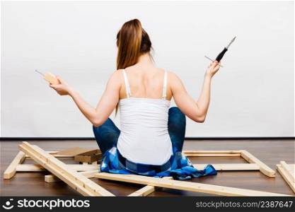 Woman assembling wooden furniture using screwdriver. DIY enthusiast. Young girl doing home improvement. Rear back view.. Woman assembling wooden furniture. DIY. Rear view.