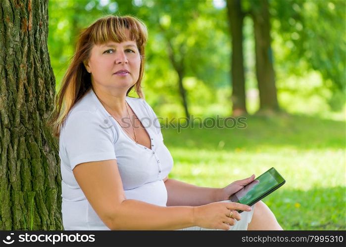 woman at a mature age in the park with a tablet resting
