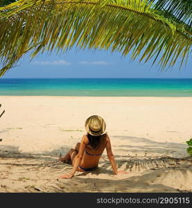 Woman at beach under palm tree with leaf shadow on her body