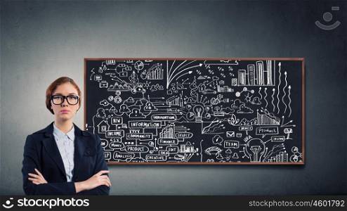 Woman at blackboard. Young confident woman wearing glasses standing near blackboard