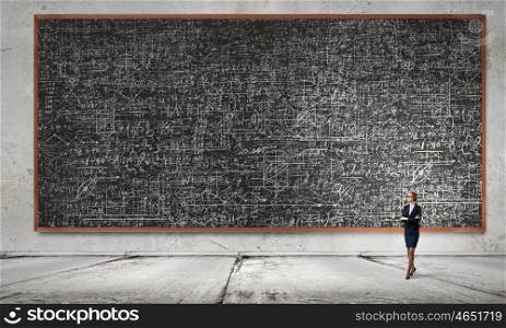 Woman at blackboard. Young confident woman wearing glasses standing near blackboard