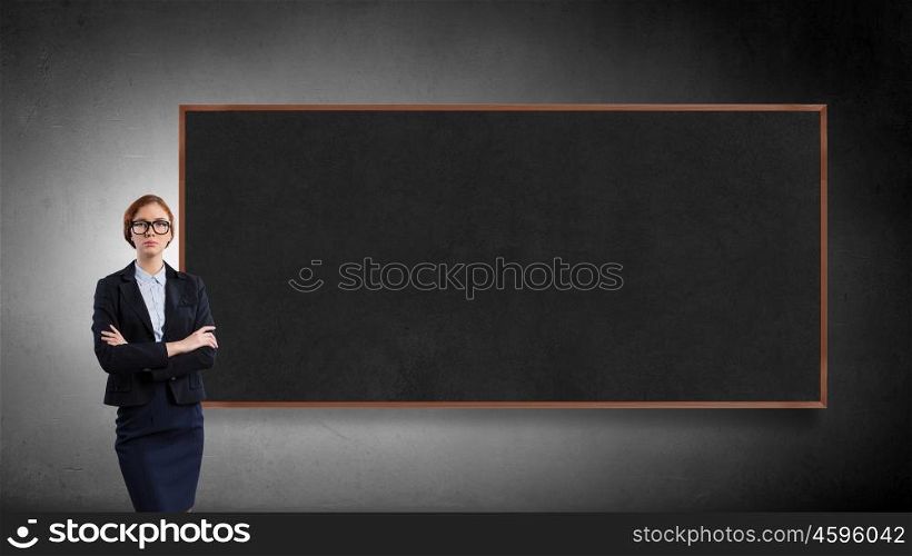 Woman at blackboard. Young confident woman wearing glasses standing near blank blackboard