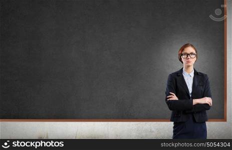Woman at blackboard. Young confident woman wearing glasses standing near blank blackboard