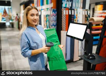 Woman at cash register sells fabric in textile store. Showcase with cloth for sewing on background, clothing patterns choice in shop. Woman at cash register sells fabric, textile store