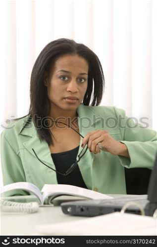 Woman at Desk Holding her Glasses