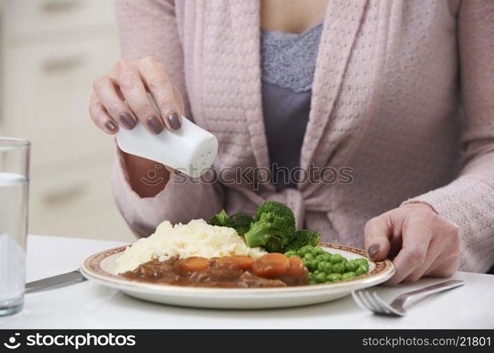 Woman At Home Adding Salt To Meal