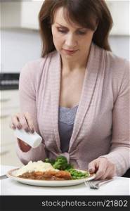 Woman At Home Adding Salt To Meal
