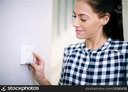 Woman At Home Adjusting Central Heating Thermostat Control