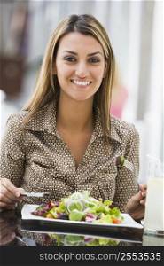Woman at restaurant eating salad and smiling (selective focus)