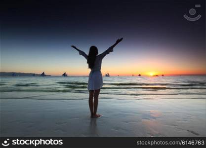 Woman at sunset by the sea. Woman with raised hands at sunset by the sea
