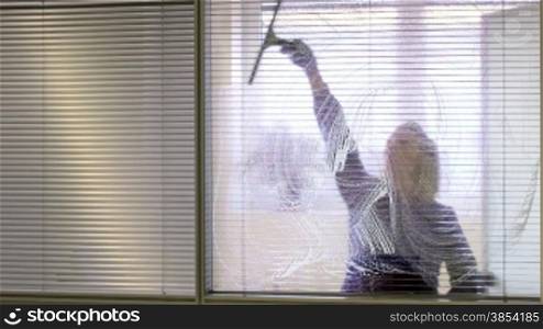 Woman at work, professional female cleaner cleaning and wiping window glass in office with detergent
