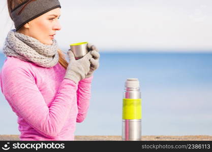 Woman athlete fit girl wearing warm sporty clothes outdoor in cold weather drinking hot tea from vacuum flask thermos, warming up. Sports, activities, hiking in winter or autumn time. Fit woman in cold day warming up drink tea