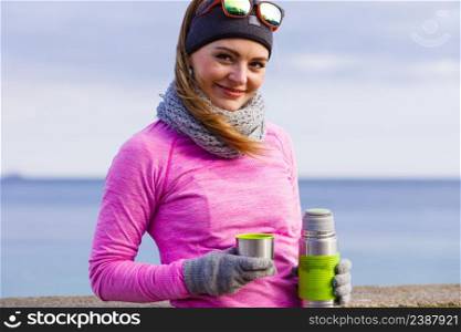 Woman athlete fit girl wearing warm sporty clothes outdoor in cold weather drinking hot tea from vacuum flask thermos, warming up. Sports, activities, hiking in winter or autumn time. Fit woman in cold day warming up drink tea