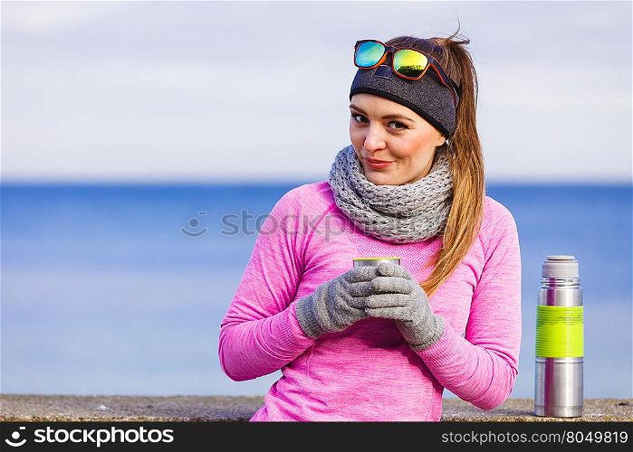 Woman athlete fit girl wearing warm sporty clothes outdoor in cold weather drinking hot tea from vacuum flask thermos, warming up. Sports, activities, hiking in winter or autumn time
