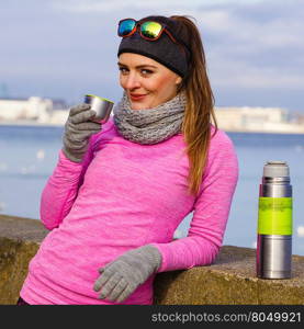 Woman athlete fit girl wearing warm sporty clothes outdoor in cold weather drinking hot tea from vacuum flask thermos, warming up. Sports, activities, hiking in winter or autumn time