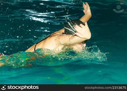 Woman athlete swimming performing butterfly style stroke in pool. Active human swimmer taking breath. Water sport comptetition.. Woman athlete swimming butterfly stroke in pool.