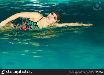 Woman athlete swimming performing crawl style stroke in pool. Active human swimmer taking breath. Water sport comptetition.. Woman athlete swimming crawl stroke in pool.