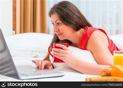 woman attentively looks at a laptop and drinking tea