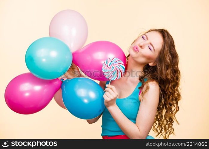 Woman attractive cheerful girl holding colorful balloons and sweet lollipop in hands. Summer holidays, celebration and happiness concept. Studio shot bright yellow background. Woman with colorful balloons and lollipop