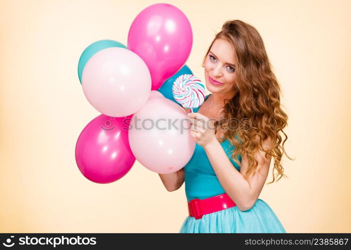 Woman attractive cheerful girl holding colorful balloons and sweet lollipop in hands. Summer holidays, celebration and happiness concept. Studio shot bright yellow background. Woman with colorful balloons and lollipop