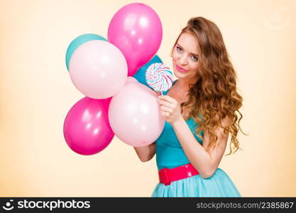 Woman attractive cheerful girl holding colorful balloons and sweet lollipop in hands. Summer holidays, celebration and happiness concept. Studio shot bright yellow background. Woman with colorful balloons and lollipop