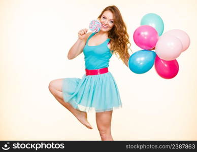 Woman attractive cheerful girl holding colorful balloons and sweet lollipop in hands. Summer holidays, celebration and happiness concept. Studio shot bright yellow background. Woman with colorful balloons and lollipop