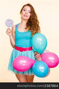 Woman attractive cheerful girl holding colorful balloons and sweet lollipop in hands. Summer holidays, celebration and happiness concept. Studio shot bright yellow background. Woman with colorful balloons and lollipop