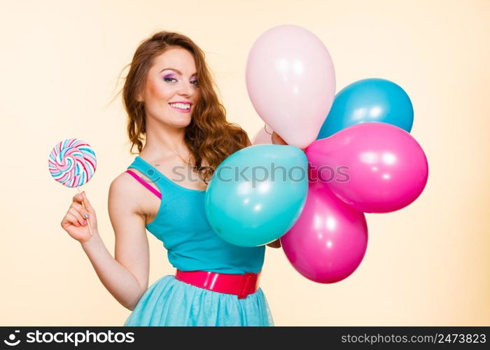 Woman attractive cheerful girl holding colorful balloons and sweet lollipop in hands. Summer holidays, celebration and happiness concept. Studio shot bright yellow background. Woman with colorful balloons and lollipop