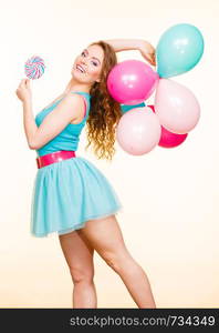 Woman attractive cheerful girl holding colorful balloons and sweet lollipop in hands. Summer holidays, celebration and happiness concept. Studio shot bright yellow background. Woman with colorful balloons and lollipop